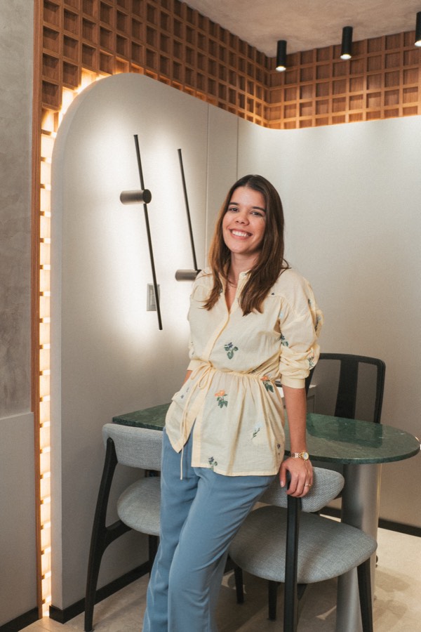 Bany Vieira sorrindo em pé numa clínica que ela projetou